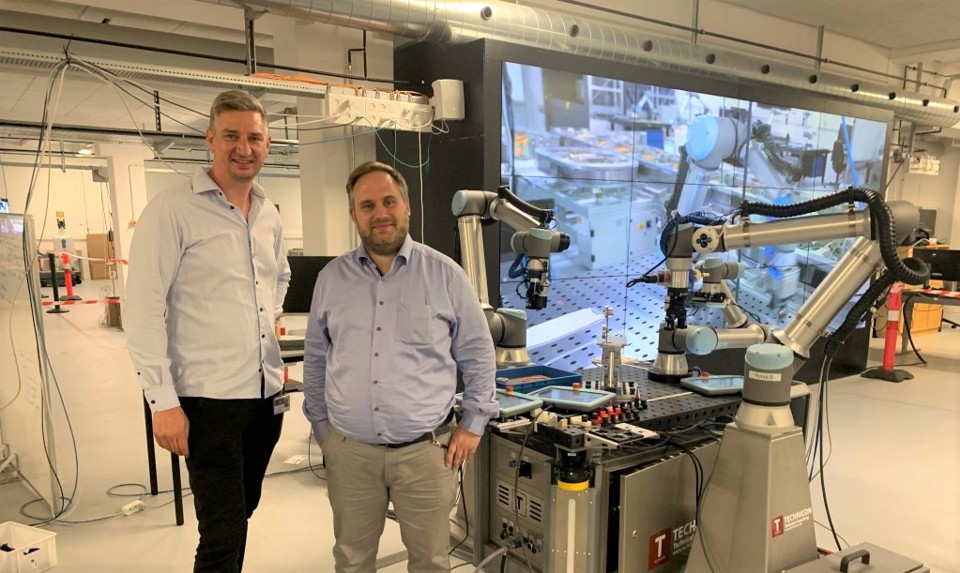 Two men next to robot, they smile at the camera